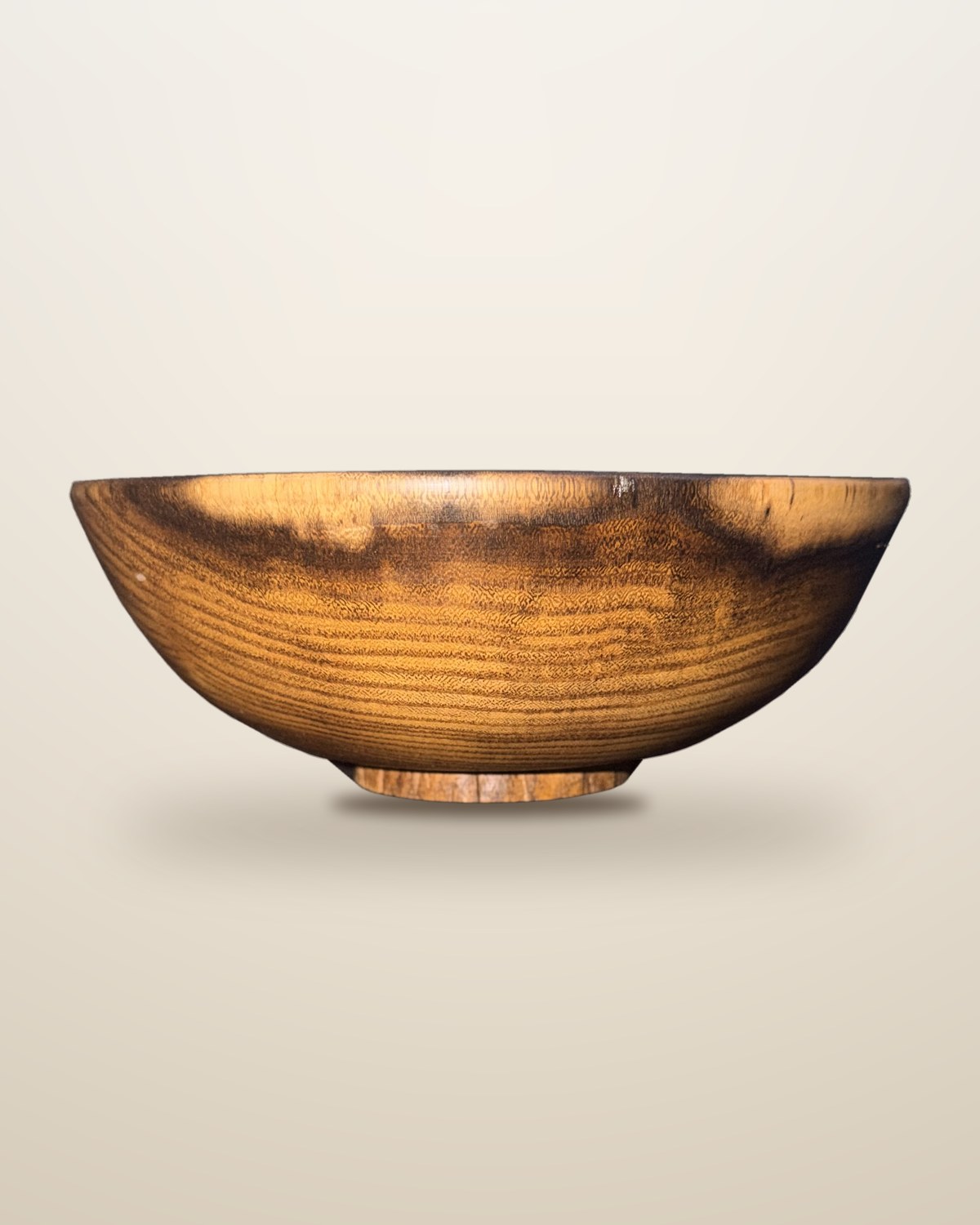 Turned acacia bowl on a small foot, close rings running round the wall and a band under the rim where the timber shifts from dark to pale